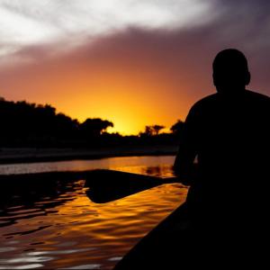 un homme assis dans un bateau dans l'eau au coucher du soleil dans l'établissement POUSADA DA DRI LODGE, à Iranduba