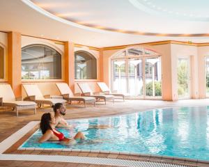 a man and a woman sitting in a swimming pool at Wellness & Genuss Resort - Engel Obertal in Baiersbronn
