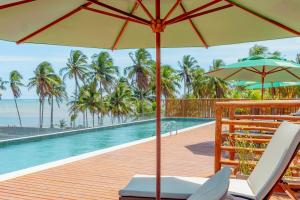 una piscina con sillas y una sombrilla junto al océano en Condomínio Essence na Beira Mar de Tatuamunha, Rota dos Milagres, en Tatuamunha