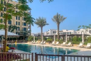 a swimming pool with chairs and palm trees and buildings at Frank Porter - Lamtara 2 in Dubai