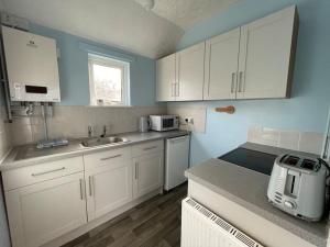 a small kitchen with white cabinets and a sink at Raes Cottage Sleeps 2 plus1 in Camelford