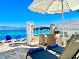 a patio with chairs and an umbrella and the ocean at Beachfront House Christina with private heatable pool by DadoVillas in Kassiopi