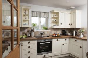 a kitchen with white cabinets and a stove top oven at Lobbs Cottage, St Mawgan in Saint Mawgan +29 photos