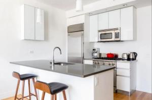 a white kitchen with a sink and two bar stools at Luxurious Studio Apartment in New York