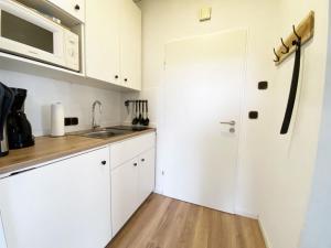 cocina con armarios blancos, fregadero y nevera en Ferien im Wangerland - Haus Wiesenweg - Apartment 2 1OG, en Horumersiel