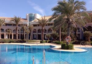 una piscina con palmeras frente a un edificio en Hotel AR Golf Almerimar en Almerimar