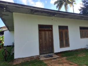 uma pequena casa branca com uma porta de madeira em Chamara home stay em Ratgama Hegoda