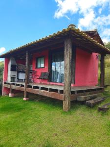 a red house with a porch on the grass at Chalés Vila Real - Tranquilidade na Serra de Carrancas - Piscina com uma vista espetacular do Pôr do Sol in Carrancas