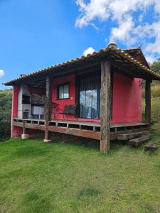 a red house with a porch on a grass field at Chalés Vila Real - Tranquilidade na Serra de Carrancas - Piscina com uma vista espetacular do Pôr do Sol in Carrancas