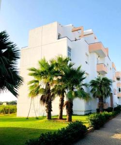 a building with palm trees in front of it at Appartement avec piscines, vue sur mer et accès à la plage à Achakar Hill, Tanger. in Tangier