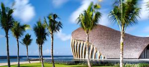 a building with palm trees in front of the ocean at The Apurva Kempinski Bali in Nusa Dua