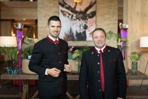 dos hombres con trajes parados uno al lado del otro en Kempinski Hotel Das Tirol, en Jochberg