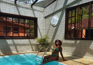a woman in a bikini sitting next to a swimming pool at Kastel Pedra Bonita in Petrópolis