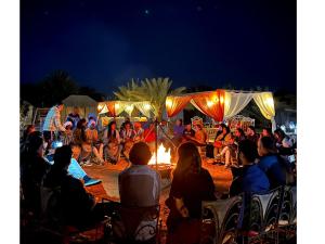 a crowd of people sitting around a fire at night at Global Luxury Camp in Merzouga