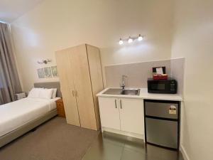 uma pequena cozinha com um lavatório e uma cama num quarto em Grand Central Serviced Apartments em Auckland
