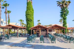 a patio with green chairs and trees and palm trees at Eurovillage Achilleas Hotel in Mastichari
