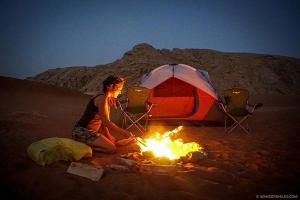 a woman is sitting next to a fire in front of a tent at Adventure Overnight Stay For Groups, Families, Couples, Foods Parties and Events Night in Dubai