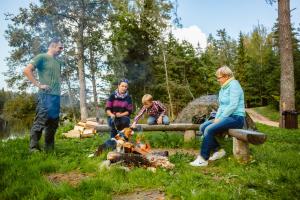 a group of people sitting around a fire with a dog at Kempings Ozolkalns in Cēsis