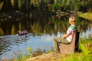 a young boy sitting on a bench by a lake at Kempings Ozolkalns in Cēsis