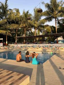 three people sitting next to a swimming pool at a resort at Off The Grid Glamps in Khopoli