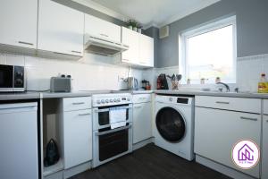 cocina con armarios blancos, lavadora y secadora en Palmers Leaze, Comfortable house close to Aztec West, en Bristol