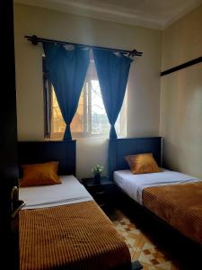 a bedroom with two beds and a window with blue curtains at Chayil Loft Mulago in Kampala