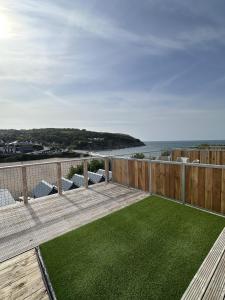 a wooden deck with a green lawn on the beach at Swn Y Mor - Sound of the Sea - by Aberporth Beach Holidays in Aberporth