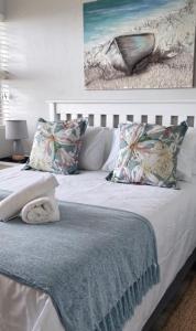 a white bed with pillows and a painting on the wall at De Valle 37 in Mossel Bay