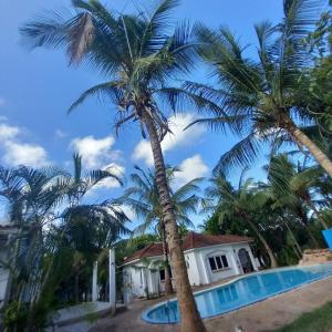 una palmera frente a una casa con piscina en Maasai Barracks Resort en Mombasa