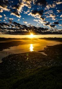 un coucher de soleil sur une étendue d'eau avec le soleil dans le ciel dans l'établissement Tromsø, à Tromsø