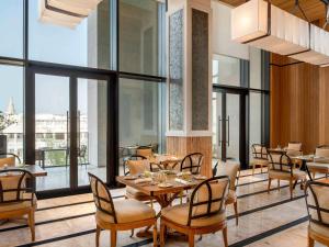 un restaurante con mesas, sillas y ventanas grandes en Alwadi Hotel Doha - MGallery, en Doha