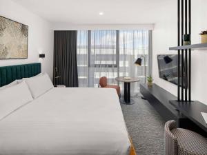 a hotel room with a large white bed and a table at The Sebel Canberra Campbell in Canberra