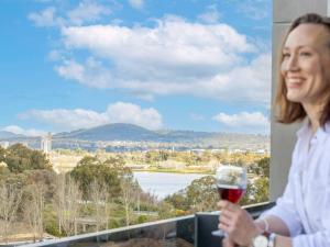 une femme tenant un verre de vin sur un balcon dans l'établissement The Sebel Canberra Campbell, à Canberra