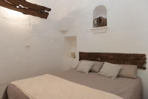 een witte slaapkamer met een bed en een houten hoofdeinde bij Trullo Nonno Marco 2.0 in Cisternino