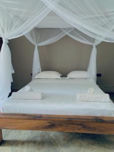 a bed with a canopy with white sheets and pillows at MAISON CARREE in Andilana