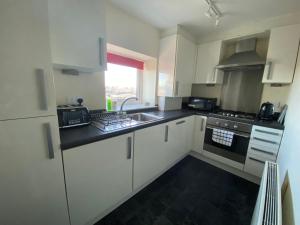 a kitchen with white cabinets and a sink at Shore Enough - Morecambe Sea Front Apartment in Heysham