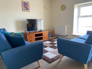 a living room with two blue chairs and a tv at Shore Enough - Morecambe Sea Front Apartment in Heysham