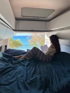 Kobieta leżąca na łóżku czytająca książkę w obiekcie Reunion in Greece Campervan w mieście Drafí