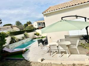 um pátio com uma mesa e um guarda-sol ao lado de uma piscina em Villa avec piscine em Montpellier