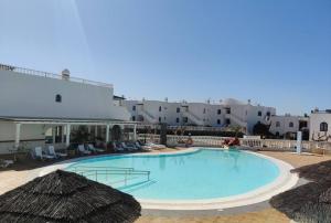 una gran piscina con sillas y sombrillas en Apartamento con piscina a 500m de la playa, en Costa Teguise
