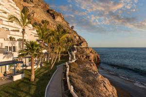 a building on a cliff next to the ocean at TUI BLUE Suite Princess - Adults Only in Taurito