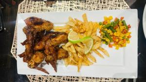 a white plate of food with french fries and vegetables at Shafas Guest House in Rundu