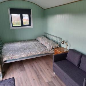 a bedroom with two beds and a couch and a window at Cwtch Winnie Shepherd's Hut- Pen Cefn Farm Holiday in Abergele