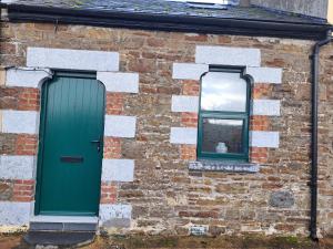 una puerta verde y dos ventanas en un edificio de ladrillo en Darrell Cottage, en Kanturk