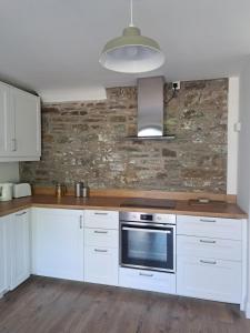cocina con armarios blancos y pared de piedra en Darrell Cottage, en Kanturk