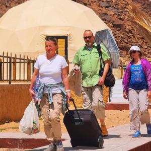 a group of people walking with luggage in front of a tent at Kylie magic camp in Wadi Rum