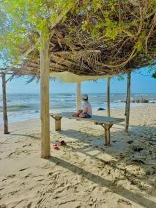 una persona sentada en un banco bajo una sombrilla en la playa en Cabaña la Gloria, en San Onofre