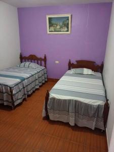 two beds in a room with purple walls and wooden floors at Casa Hospedaje Aromas in Tarapoto