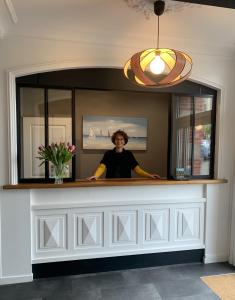 a woman standing behind a counter with a mirror at Hôtel de France in Pléneuf-Val-André