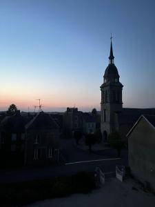 une église avec une tour avec une cloche à crépuscule dans l'établissement Maison d'hôtes La Doucelle, à Lignieres-Orgeres